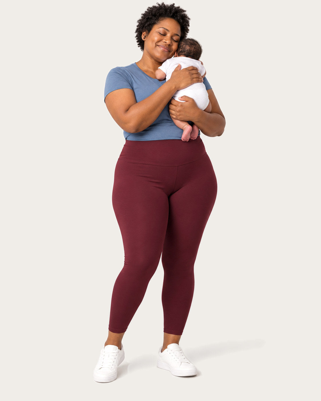 New mom in burgundy postpartum leggings holding her newborn against her shoulder
