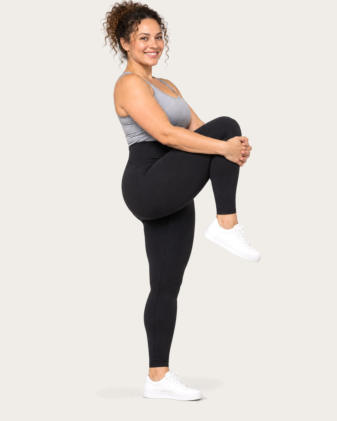 Mom hugging one knee to her chest in black postpartum leggings