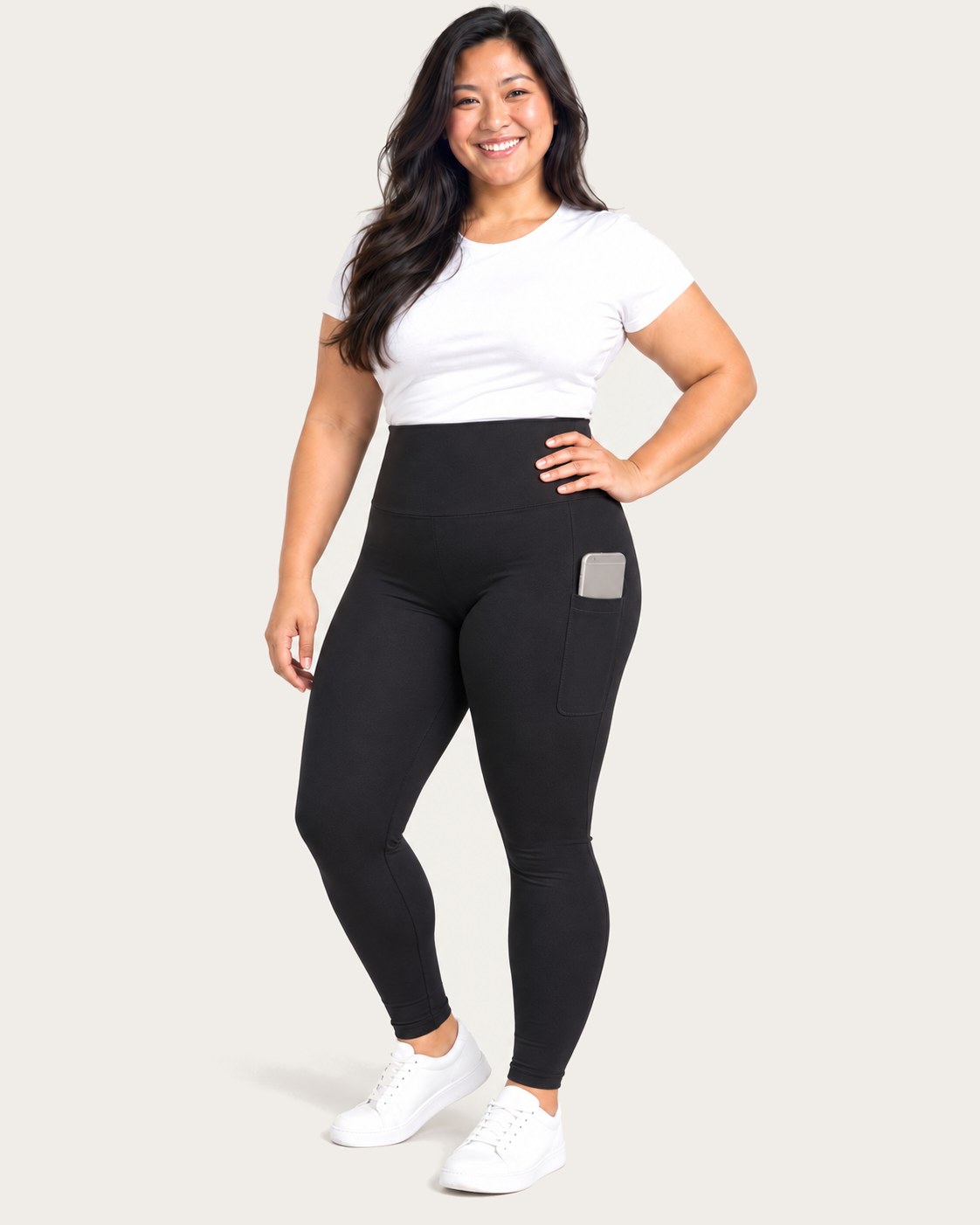 Smiling mom standing tall in black high-waisted postpartum leggings, her phone in the side pocket