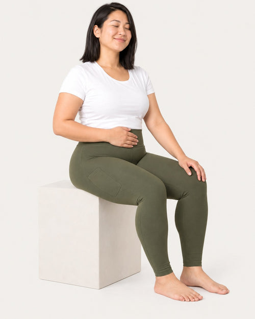 Mom sitting in olive green leggings, one hand resting on the high waistband