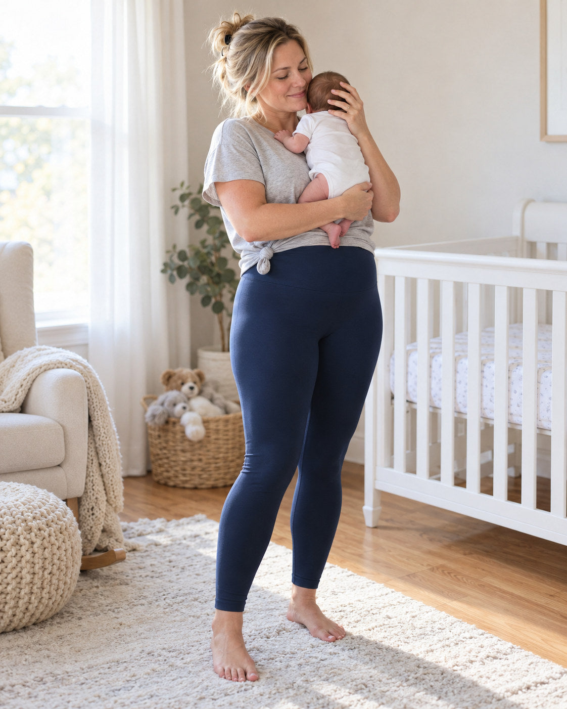 Mom in midnight blue leggings rocking her newborn beside the crib