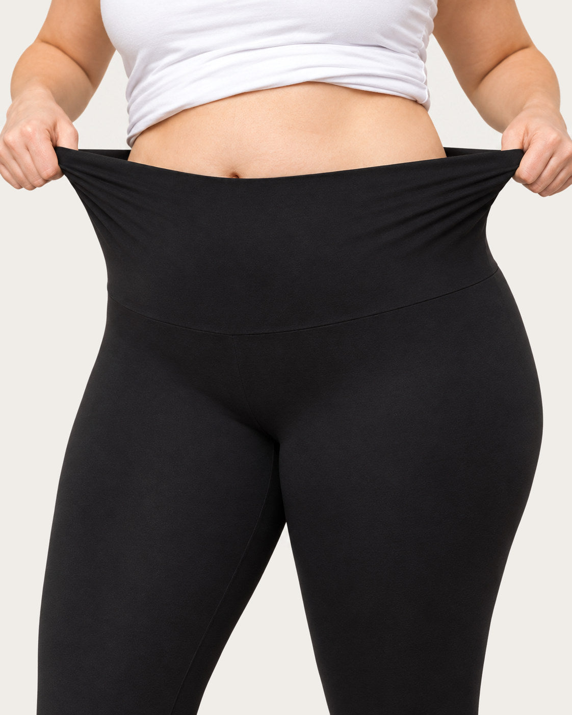 Two hands stretching the wide waistband of black leggings