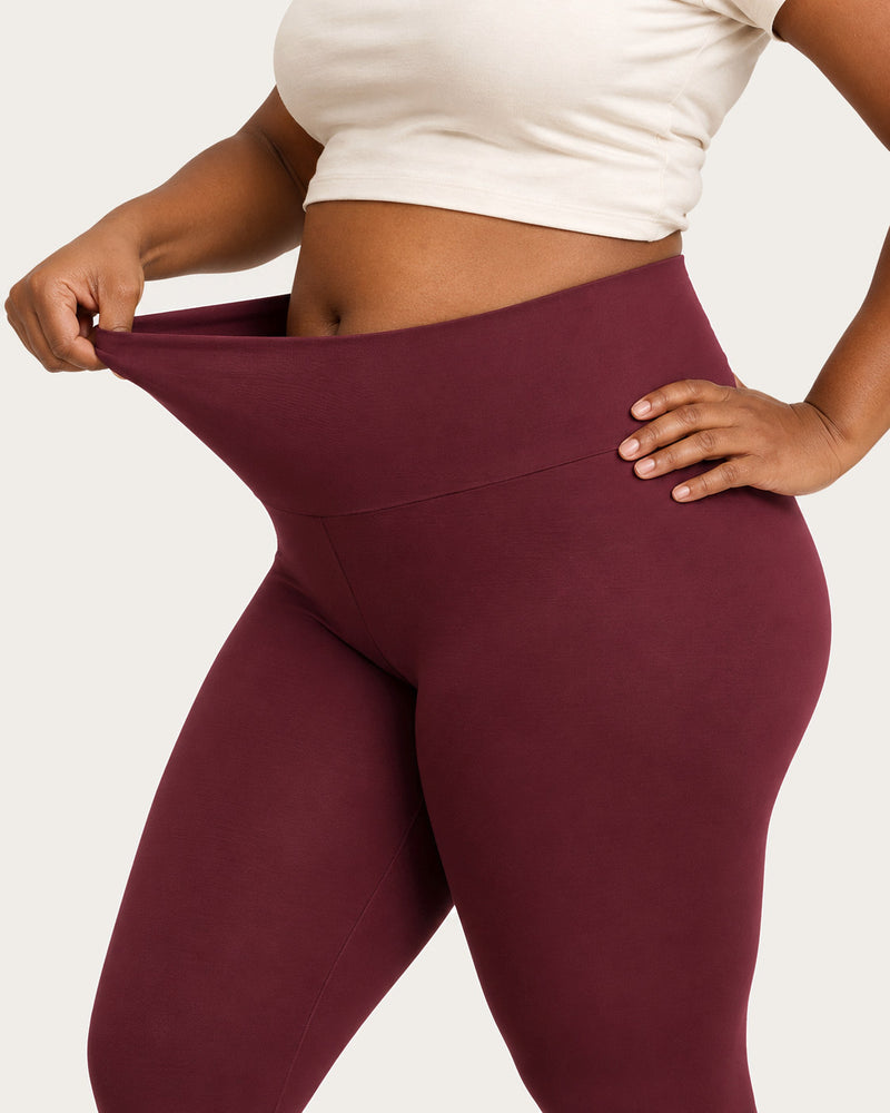 Hand pulling the waistband of burgundy leggings forward to show the stretch