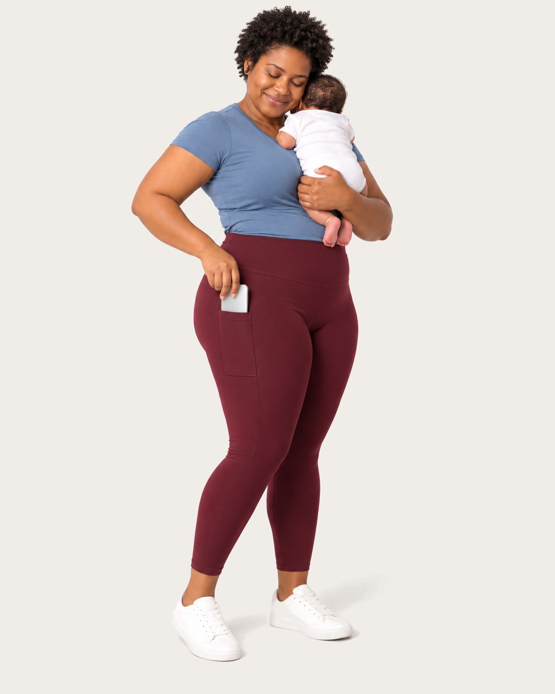 Mom holding her newborn, her phone tucked in the side pocket of her burgundy leggings
